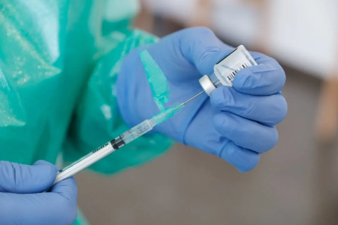 Mano con guante sanitario sosteniendo una jeringuilla y un vial de vacuna