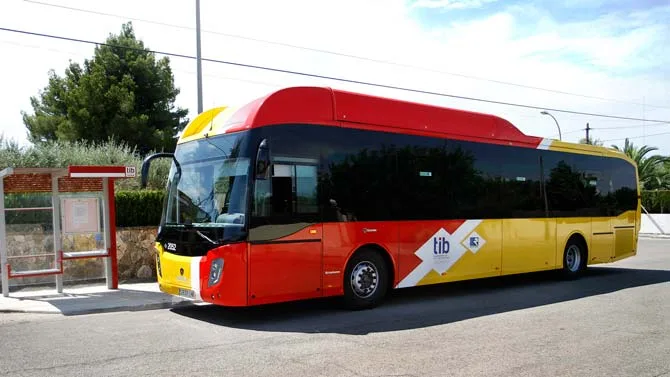 Autobús de color rojo y amarillo de la red TIB circulando por una carretera en Mallorca