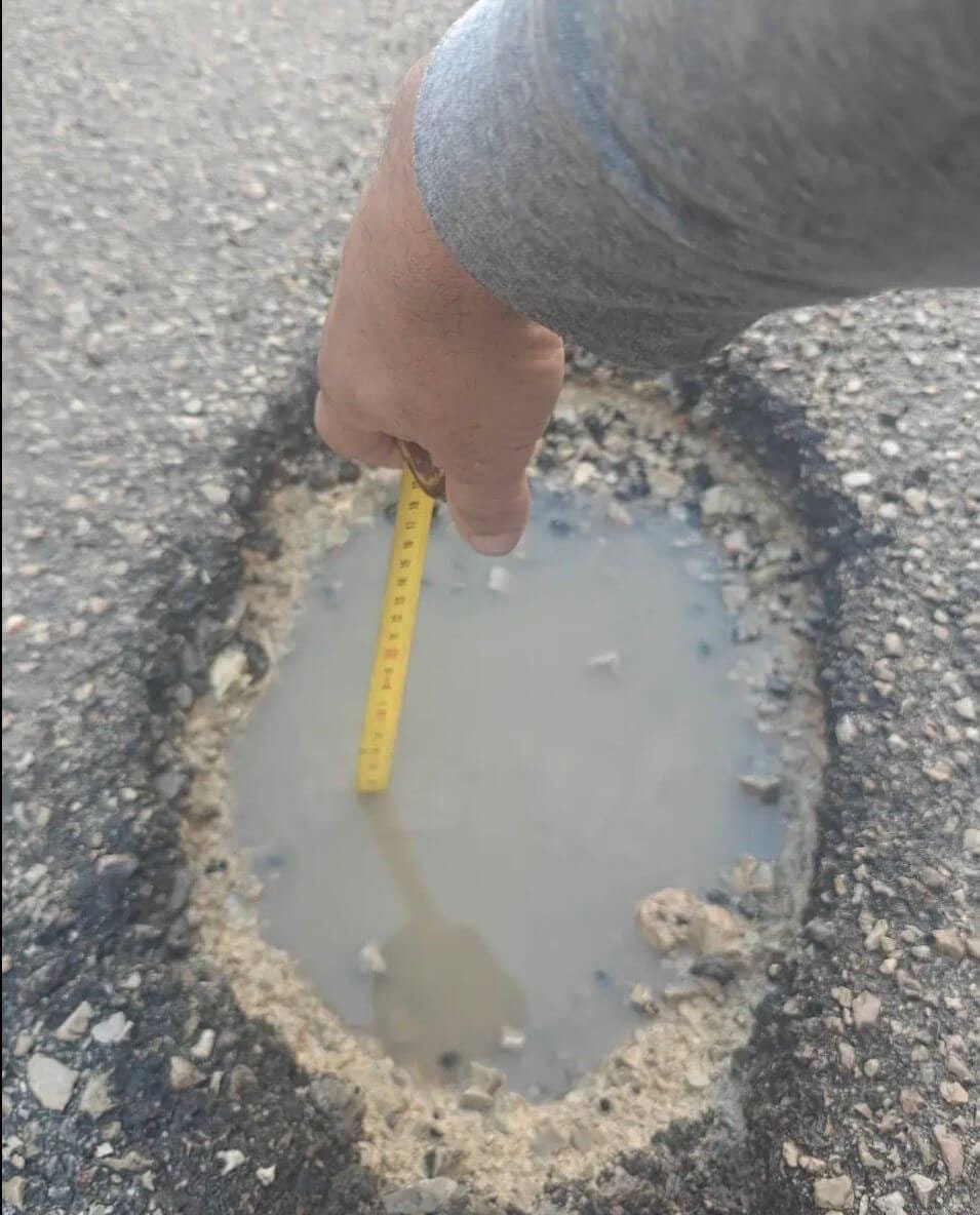 Una persona mide con una cinta métrica la profundidad de un bache lleno de agua en una calle de Manacor