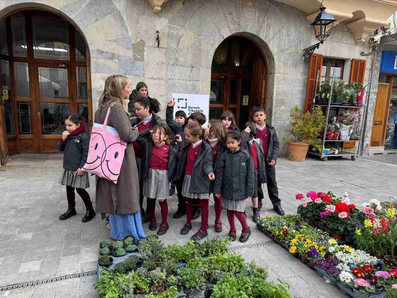 Grupo de escolares de Inca observando flores en el Mercado del Jueves frente a un edificio municipal