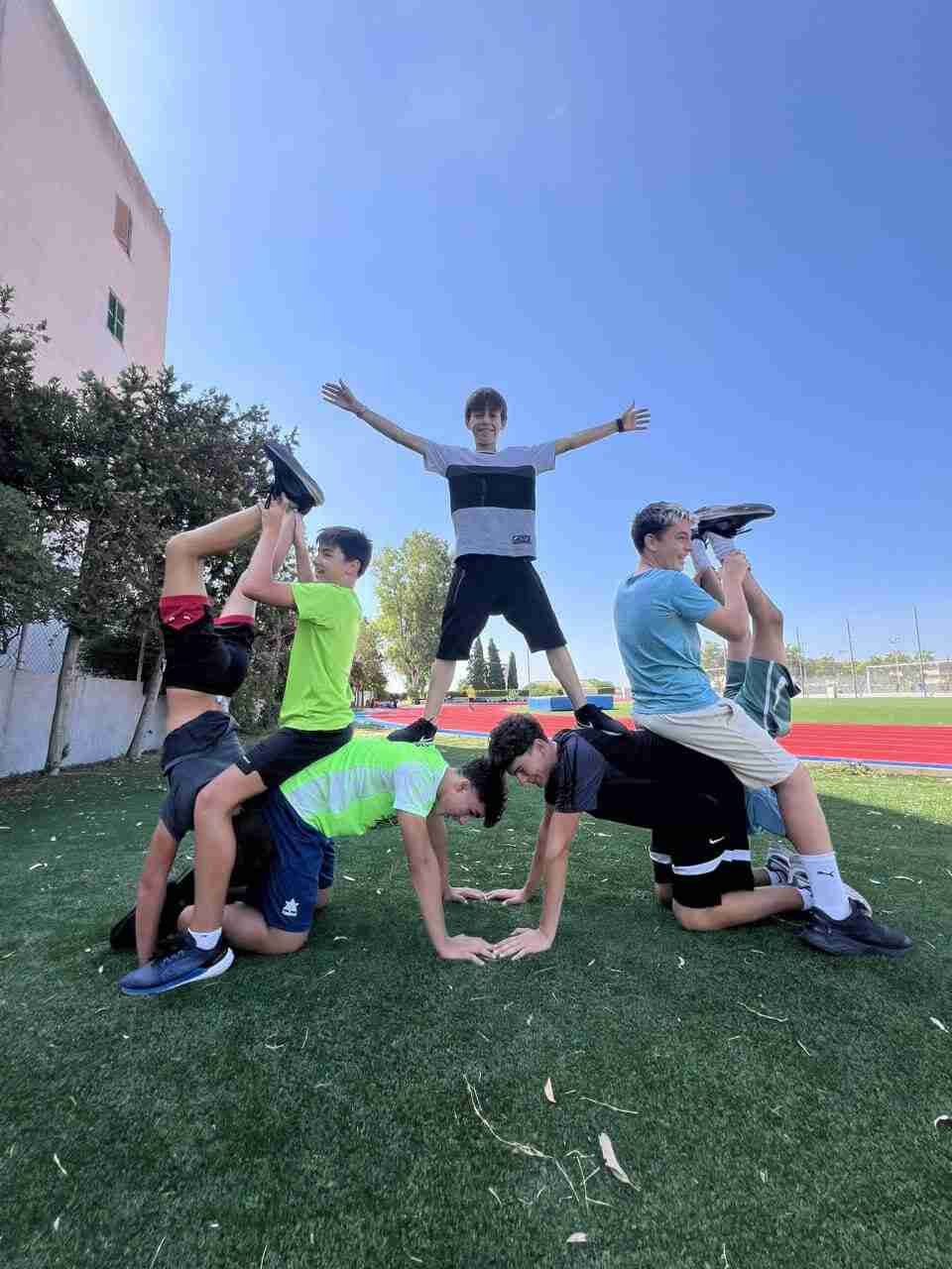 Un grupo de jóvenes realizando una pirámide humana y ejercicios de equilibrio sobre césped artificial