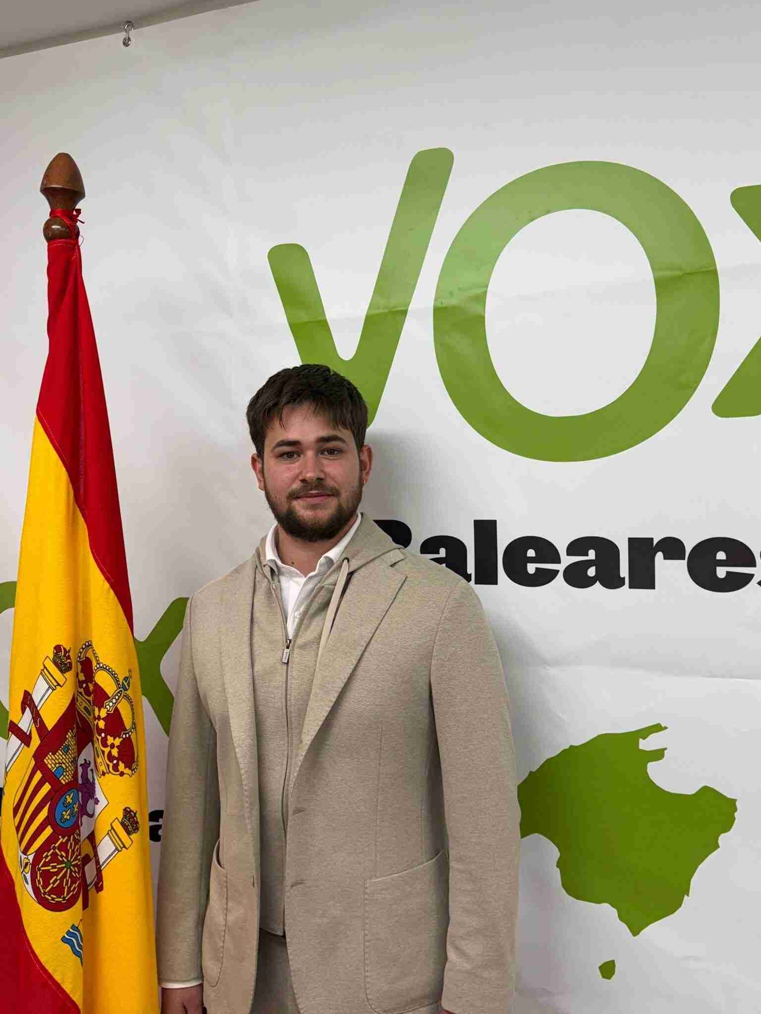 Nicolás Rodríguez posando ante el logotipo de VOX Baleares y la bandera de España