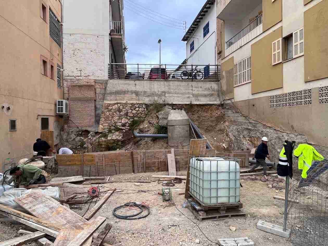 Operarios trabajando en la base de un talud de tierra y piedra entre edificios en Porto Cristo