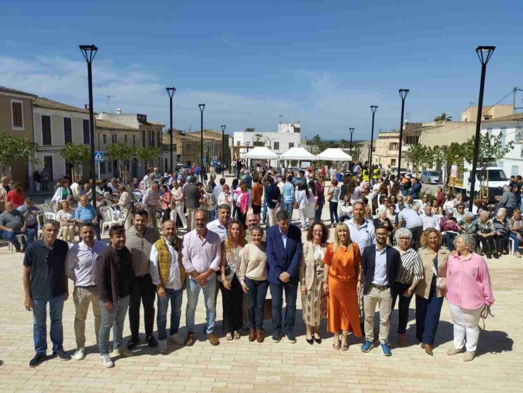 Foto de grupo de las autoridades municipales y autonómicas en la nueva plaza con vecinos de Cas Concos al fondo
