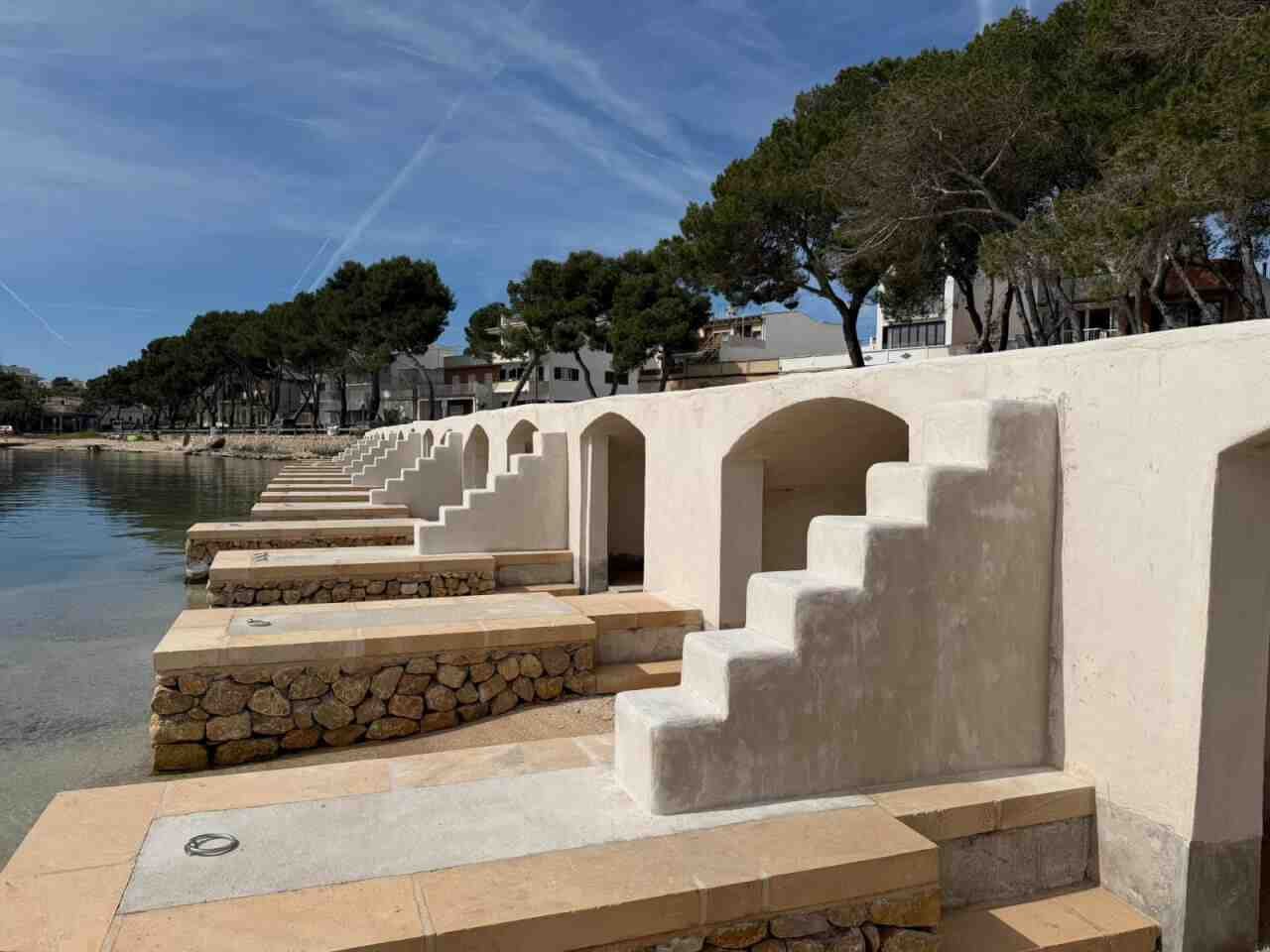 Estructuras de escars rehabilitadas en el puerto de Portocolom con paredes blancas y mar en calma