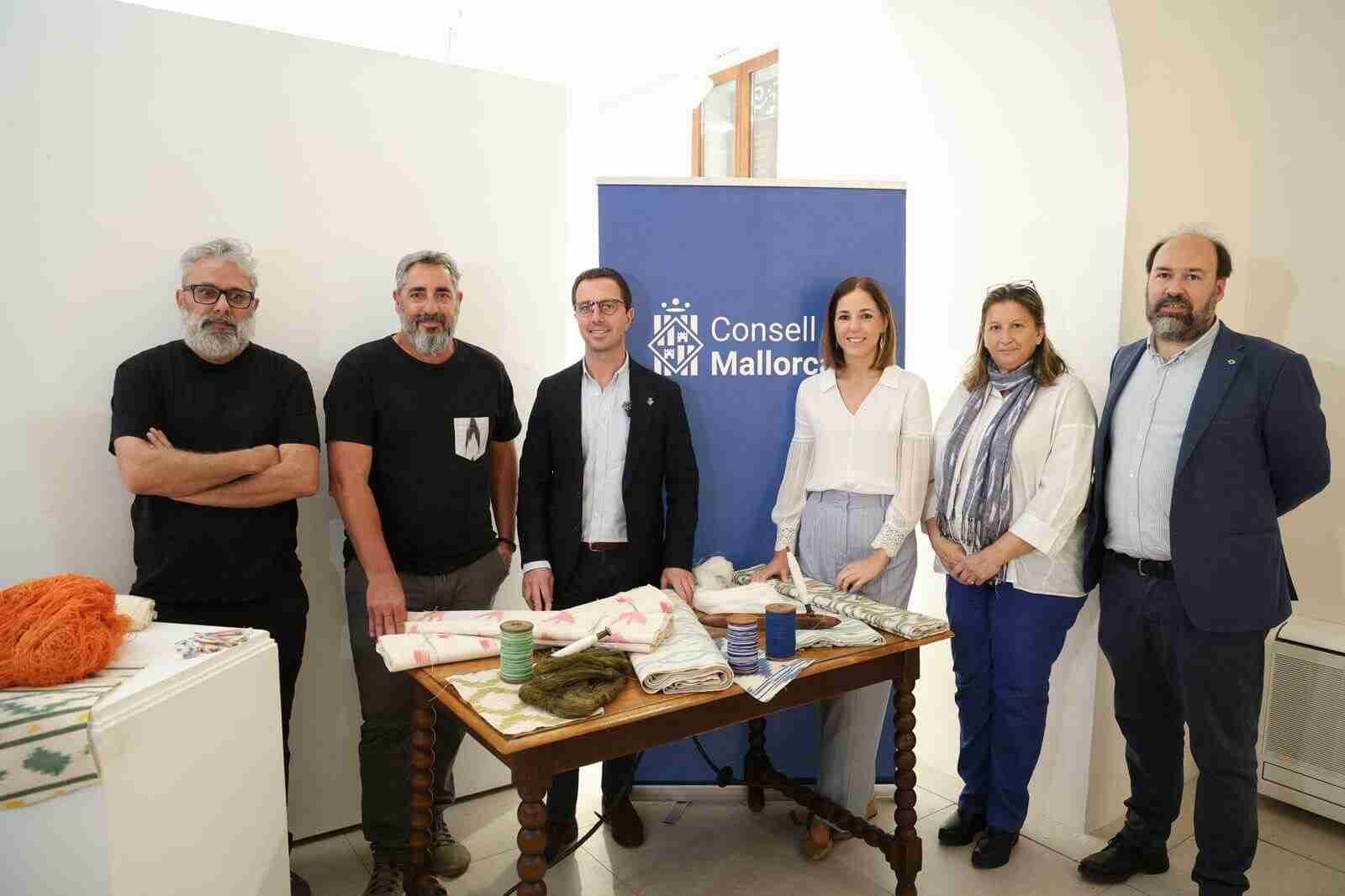 Autoridades del Consell de Mallorca y artesanos textiles junto a una mesa con muestras de tela de llengües
