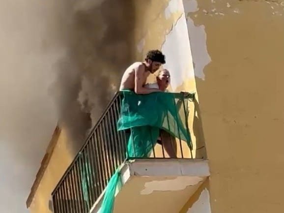 Primer plano de dos supuestos okupas pidiendo auxilio desde un balcón invadido por el humo negro en Cala Millor