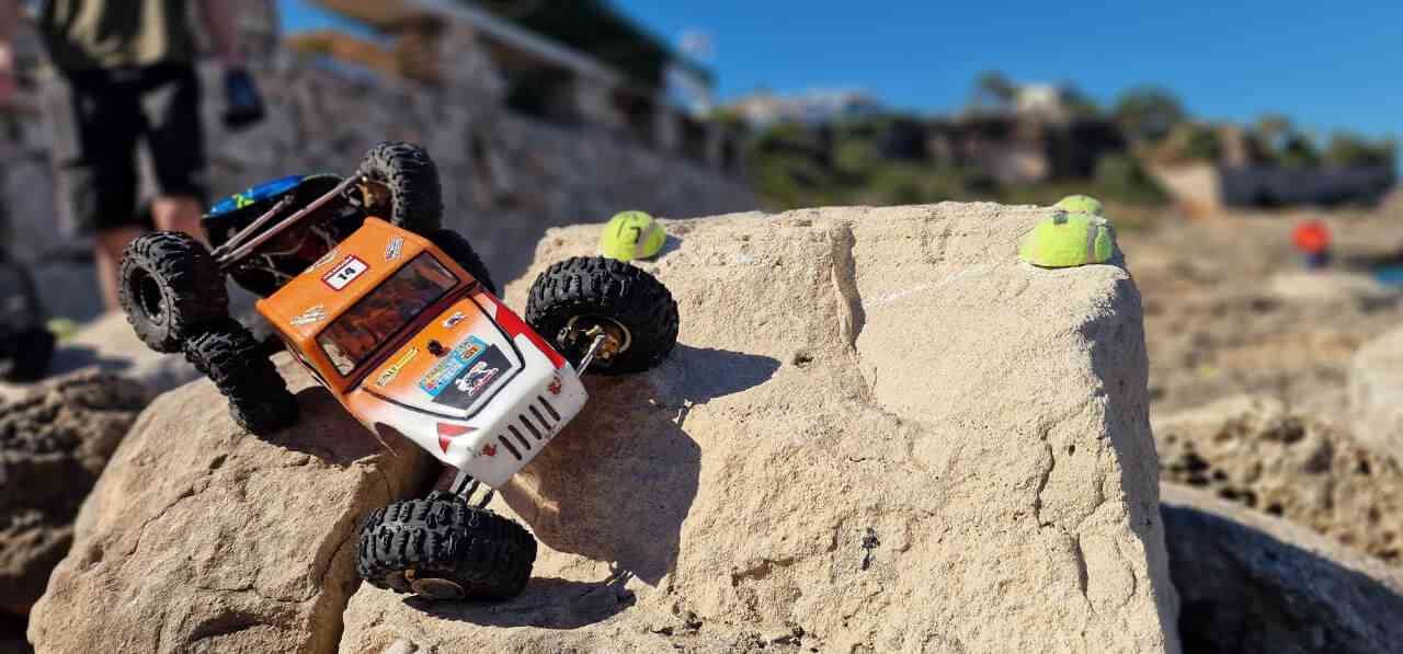 Un coche de radiocontrol crawler de color naranja y blanco superando una gran roca en Cala Murada durante el Campeonato Balear