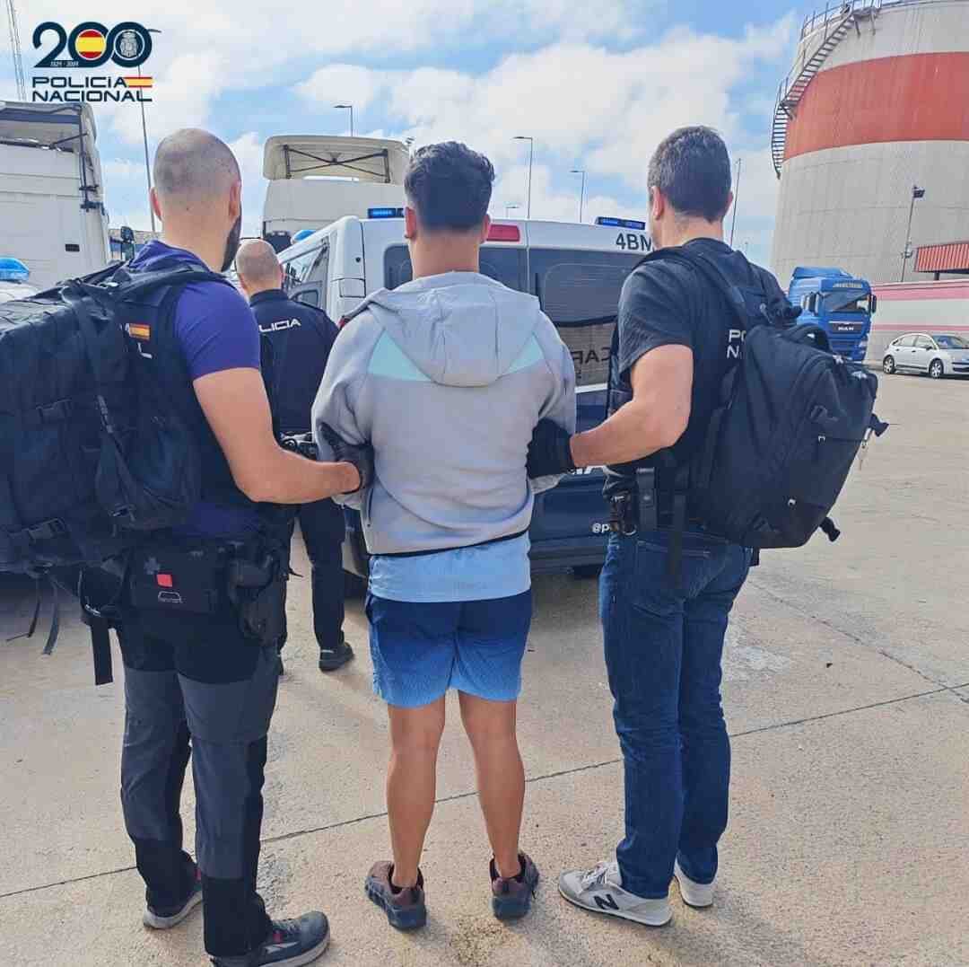 Dos agentes de la Policía Nacional de la comisaría de Manacor de espaldas custodian a un implicado extranjero esposado junto a una furgoneta policial en el exterior
