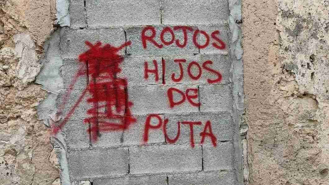 Primer plano del insulto "Rojos hijos de puta" pintado en spray rojo sobre una pared de bloques