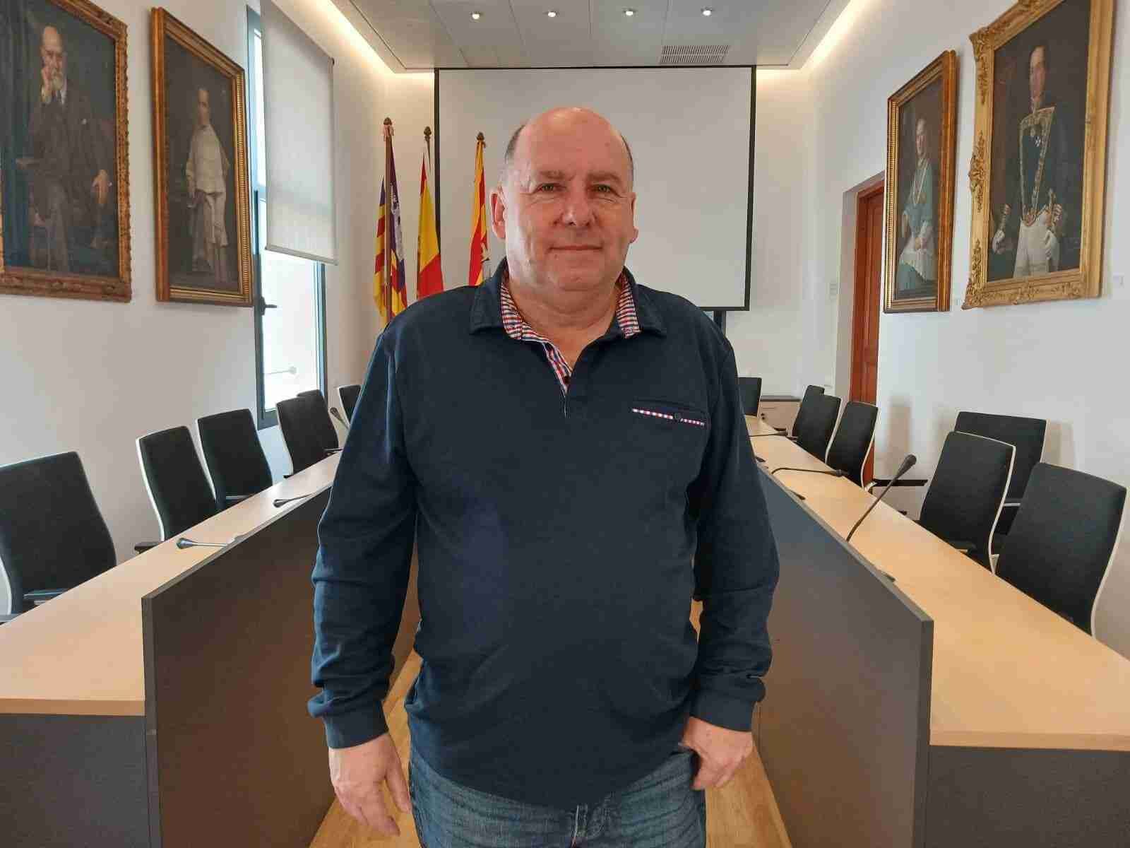 Retrato individual del periodista Gori Vicens Julià posando en la sala de plenos del Ayuntamiento de Felanitx ante la mesa de juntas y los retratos oficiales