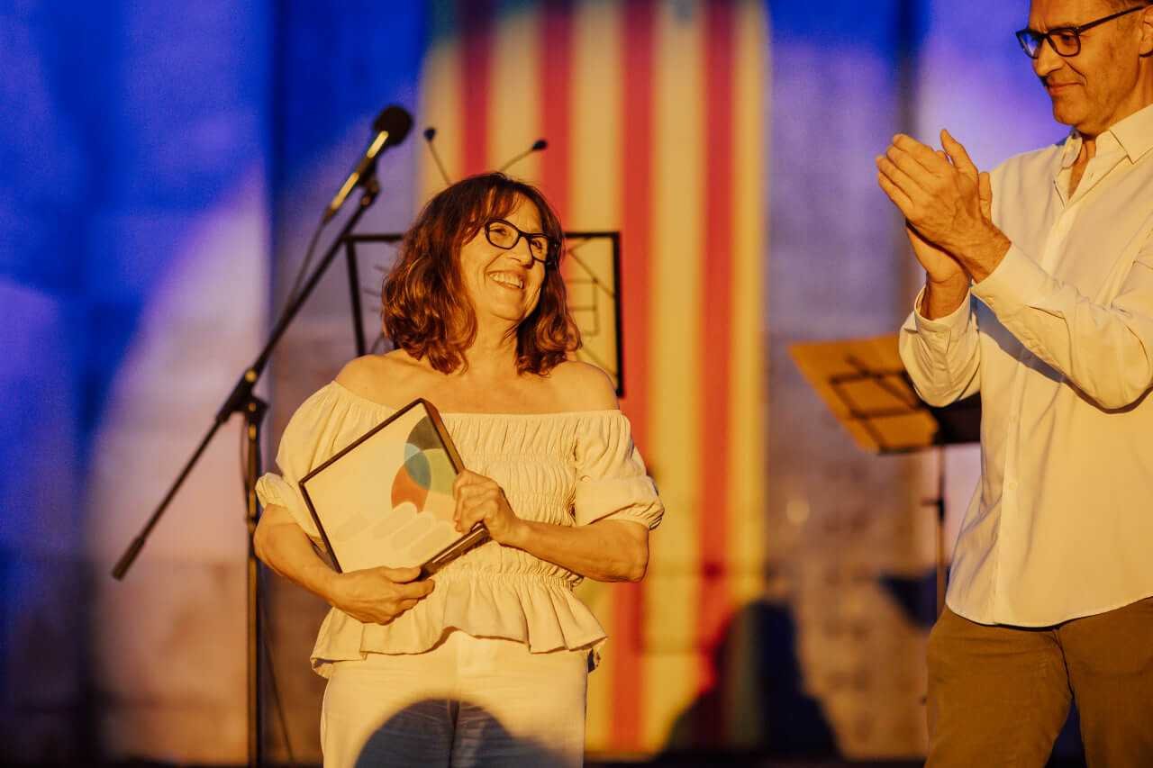 Rosa Sunyer sonríe en el escenario sosteniendo la baldosa hidráulica institucional junto al alcalde Miquel Oliver que la aplaude.