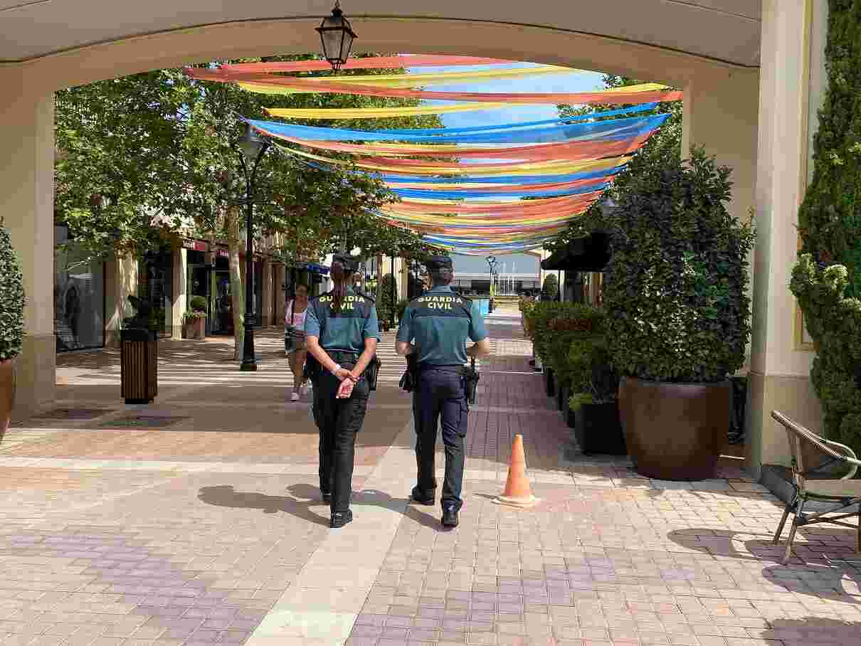 Dos agentes de la Guardia Civil patrullando de espaldas por un paseo peatonal del Mallorca Fashion Outlet engalanado con cintas de colores
