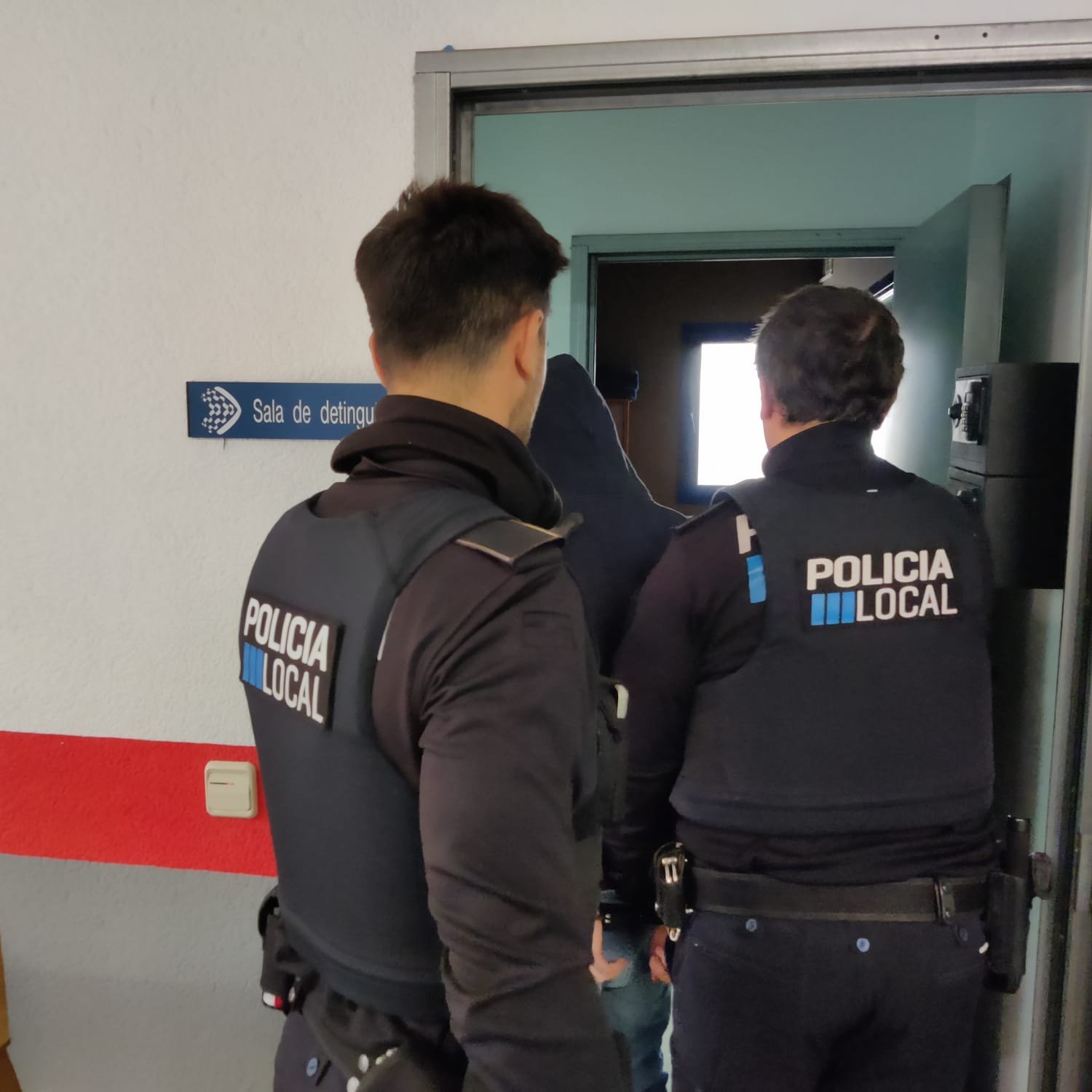Dos policías locales de Sant Llorenç escoltan a un detenido con capucha hacia la sala de detenidos