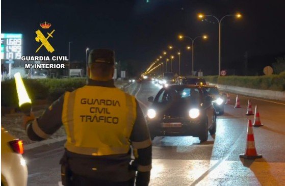 Un agente de la Guardia Civil de Tráfico de espaldas con chaleco reflectante dirigiendo el paso de vehículos por la noche en Baleares