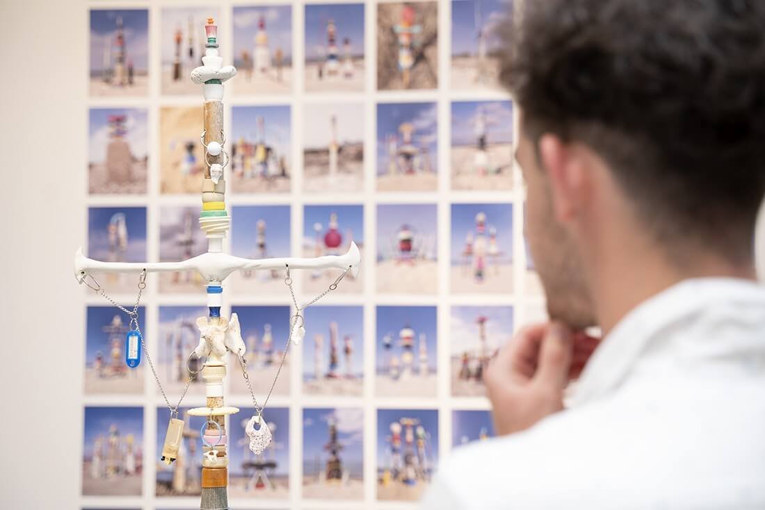Un hombre observa la escultura y el mosaico de fotografías de la obra Altares y tótems playeros de Julià Panadès