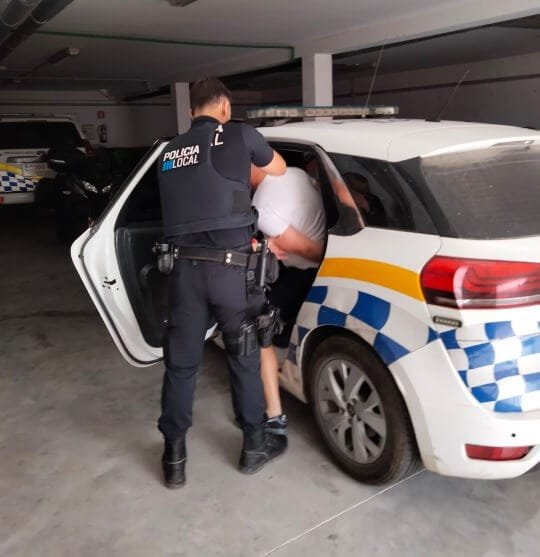 Un agente de la Policía Local introduce a uno de los implicados de camiseta blanca en la parte trasera de un coche patrulla oficial