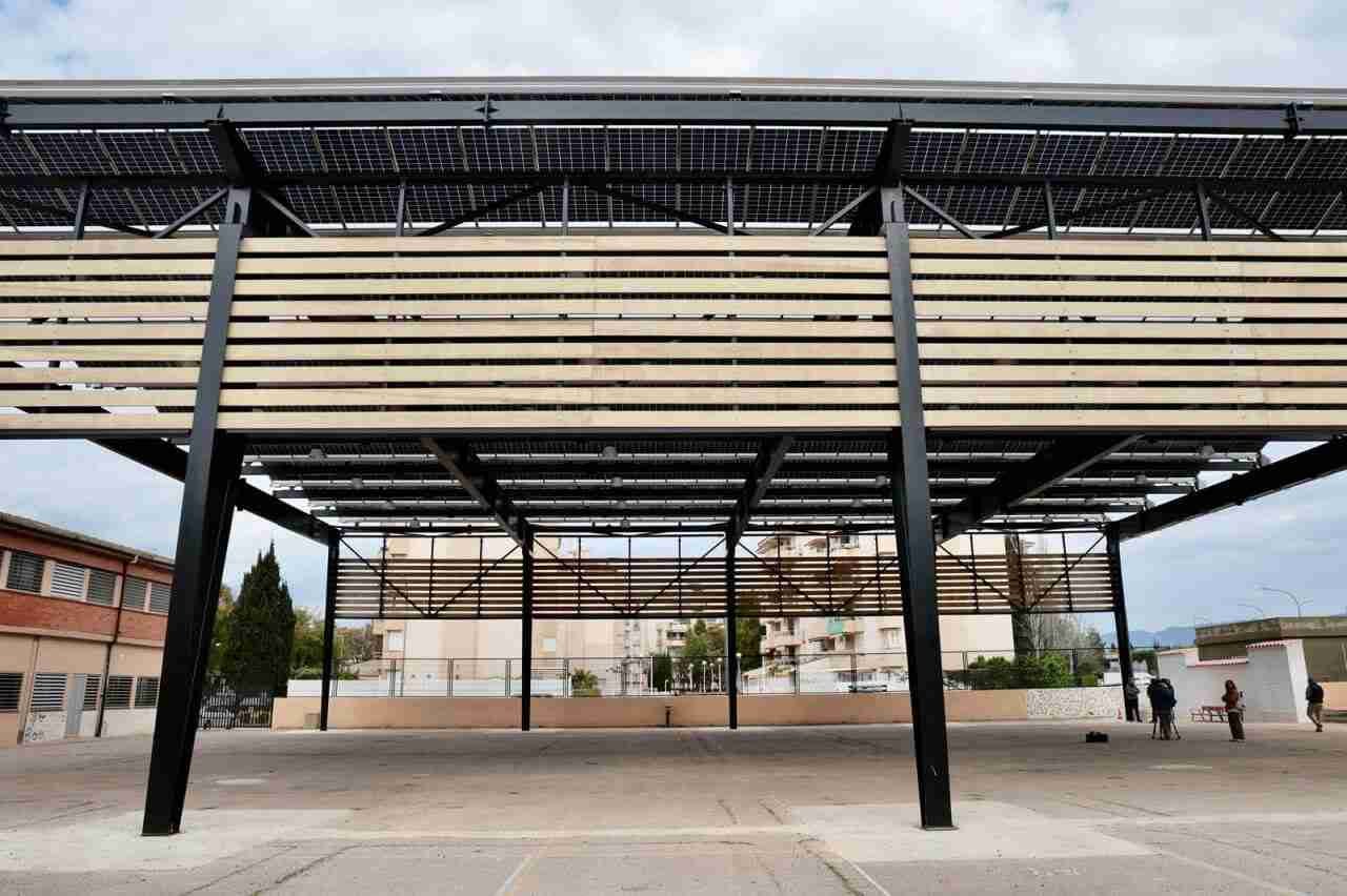 Gran estructura metálica con techado de rejilla y lamas de madera horizontales instalada en un patio o plaza pública