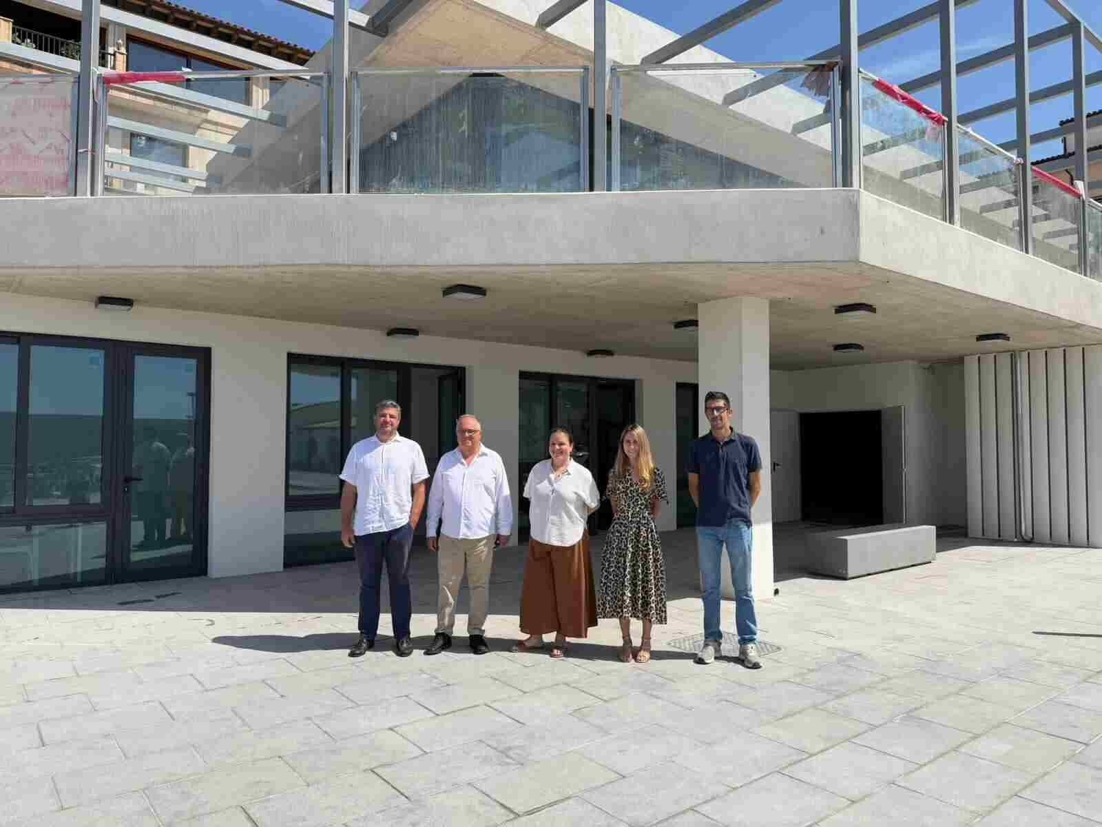 Cinco autoridades posando frente a la fachada del nuevo edificio multiusos de paredes blancas y cristaleras en el puerto de Cala Rajada