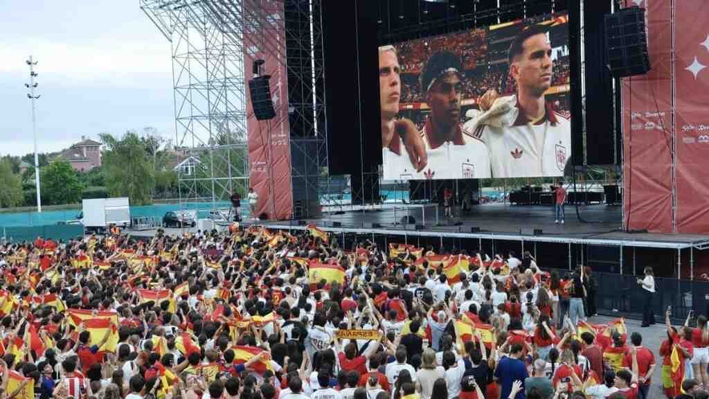 Cientos de aficionados con camisetas rojas y banderas de España frente a una pantalla gigante de televisión
