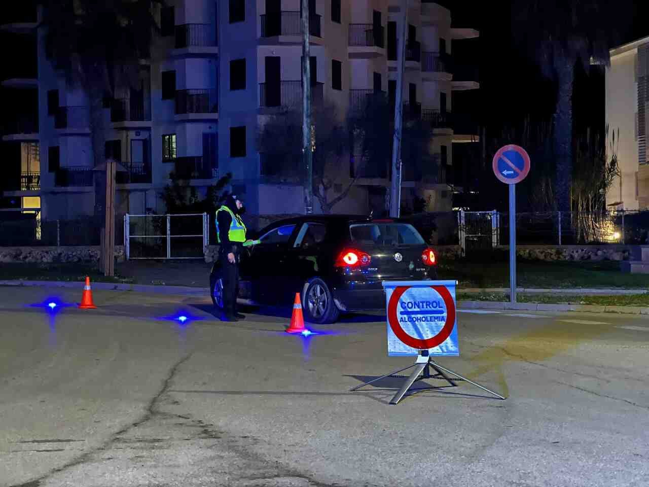 Agente de la Policía Local de Felanitx inspeccionando un vehículo negro de noche junto a un cartel circular de control de alcoholemia