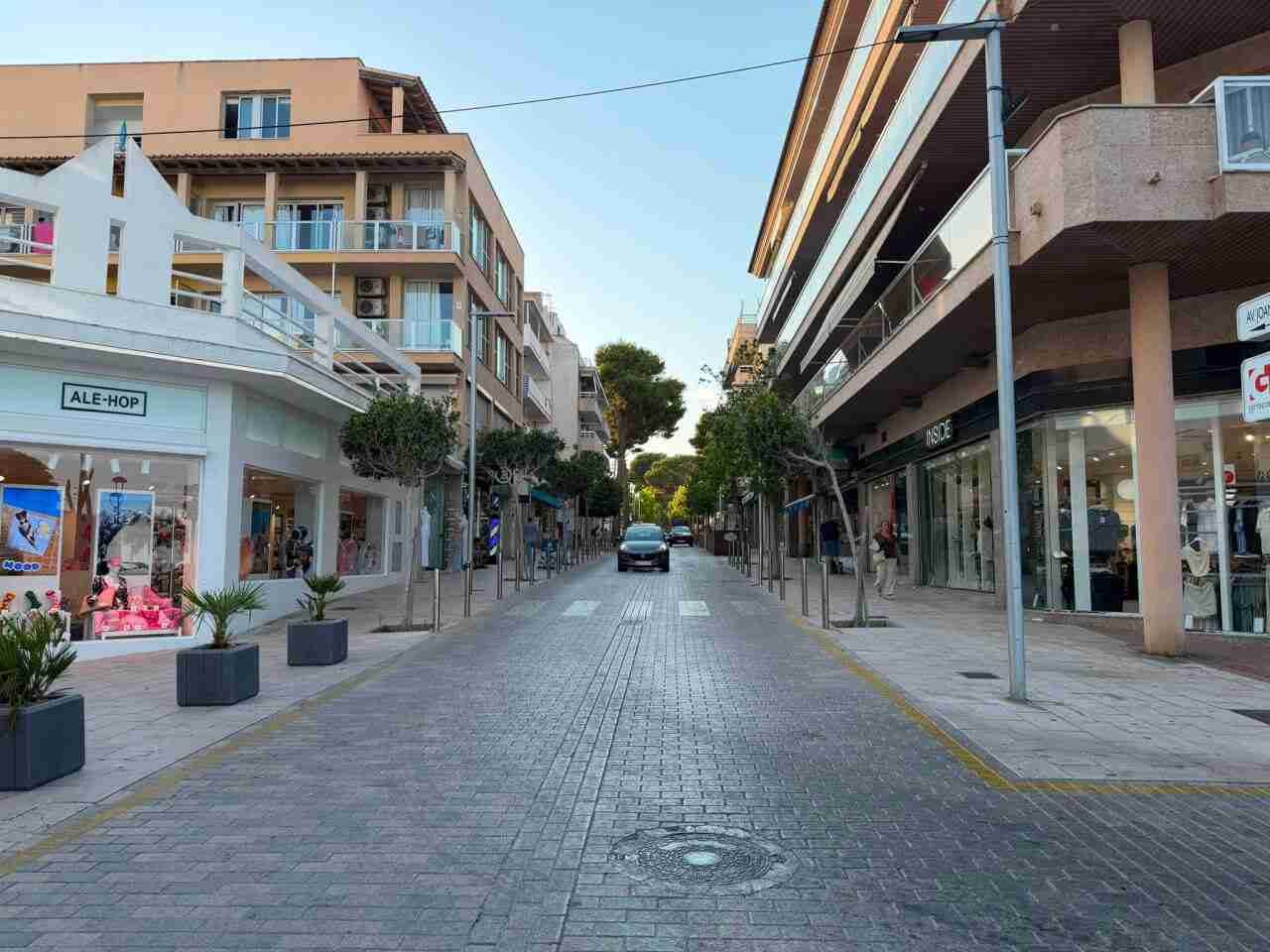 Vista general de la avenida Juan Servera Camps de Cala Millor con comercios a ambos lados y un coche circulando al fondo