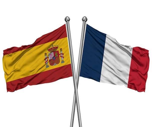 Las banderas oficiales de España y Francia ondeando juntas sobre mástiles cromados cruzados con fondo blanco