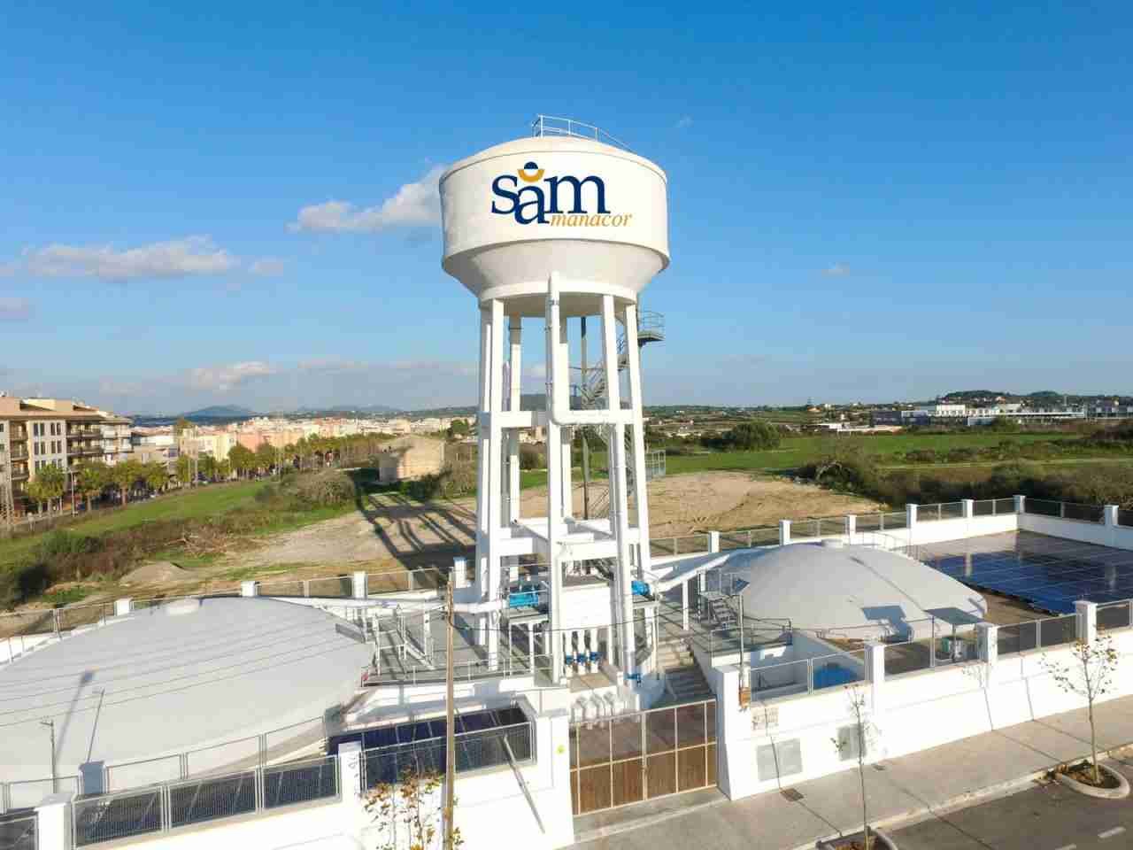 Depósito elevado de agua blanco con el logotipo azul de SAM Manacor rodeado de depósitos y placas solares