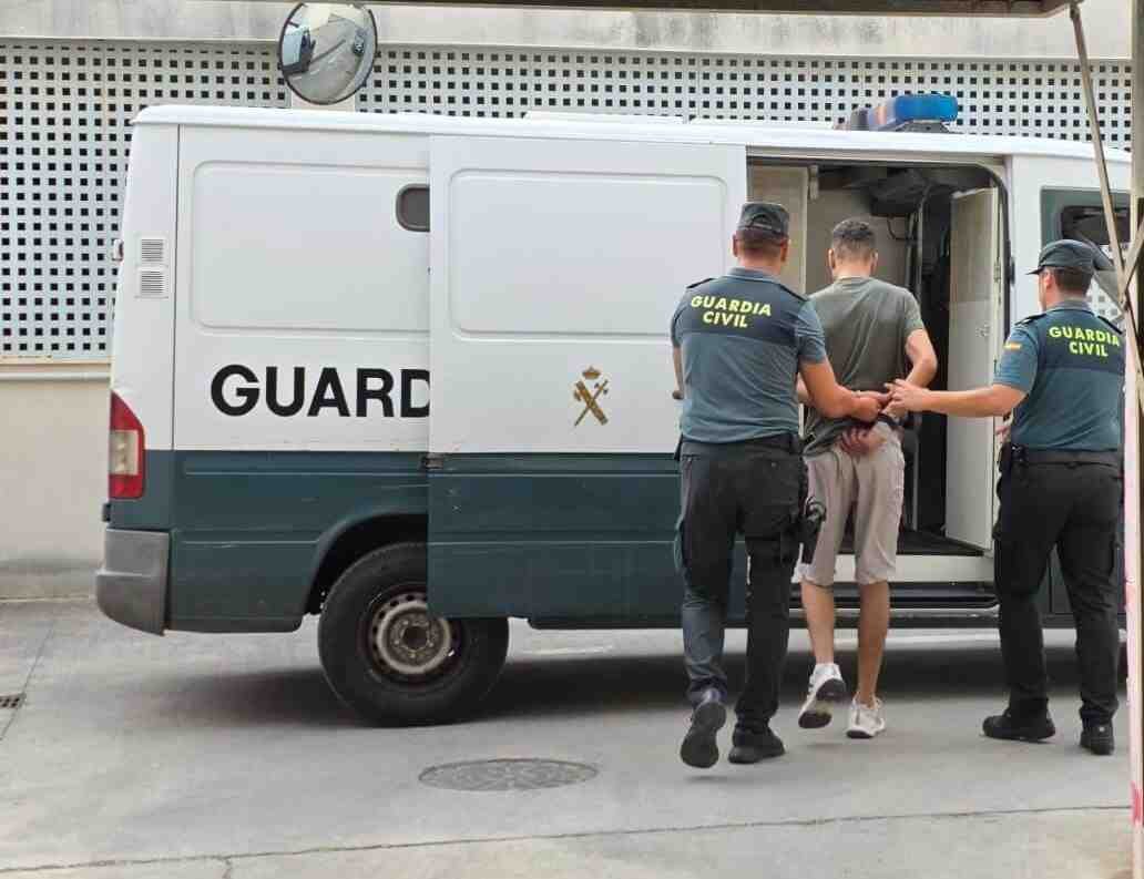 Dos agentes de la Guardia Civil escoltan de espaldas a un magrebí esposado hacia el interior de un furgón policial