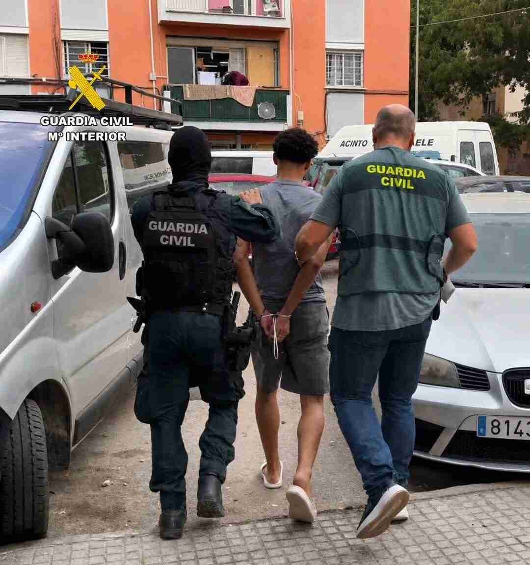 Agentes de la Guardia Civil escoltan a un individuo esposado entre vehículos aparcados en la calle
