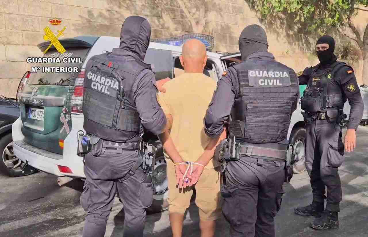 Dos agentes de la Guardia Civil custodian por la espalda a uno de los delincuentes esposado junto a un coche oficial