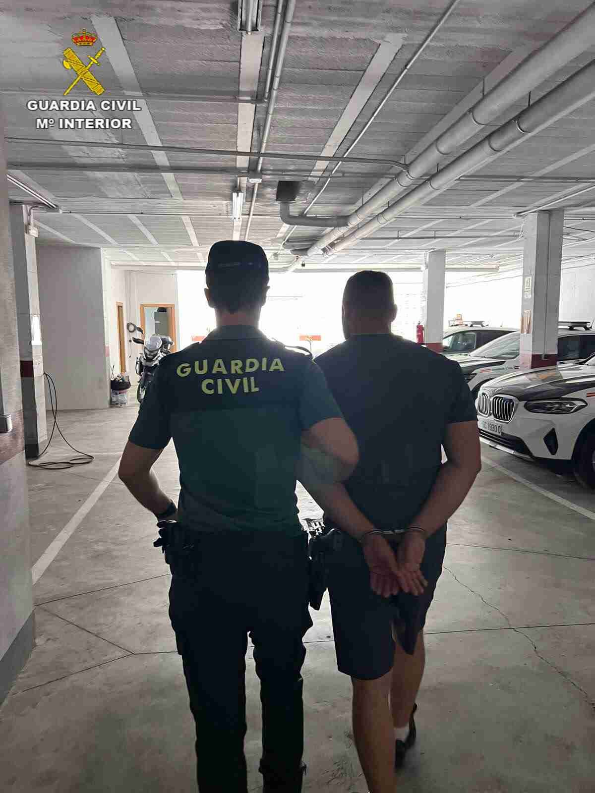 Vista trasera de un agente de la Guardia Civil conduciendo a un individuo esposado por el garaje de las dependencias policiales