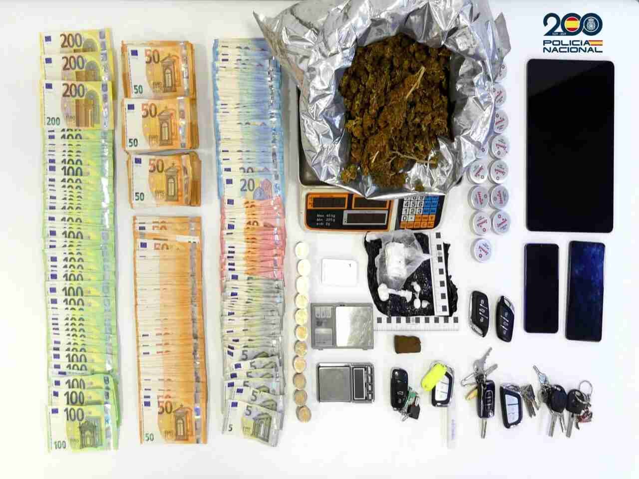 Fajos de billetes de euro ordenados por valor, cogollos de marihuana sobre una báscula, dosis de cocaína en envoltorios plásticos, una pieza de hachís, básculas de precisión, una tableta electrónica, teléfonos móviles y varios juegos de llaves expuestos por la Policía Naciona