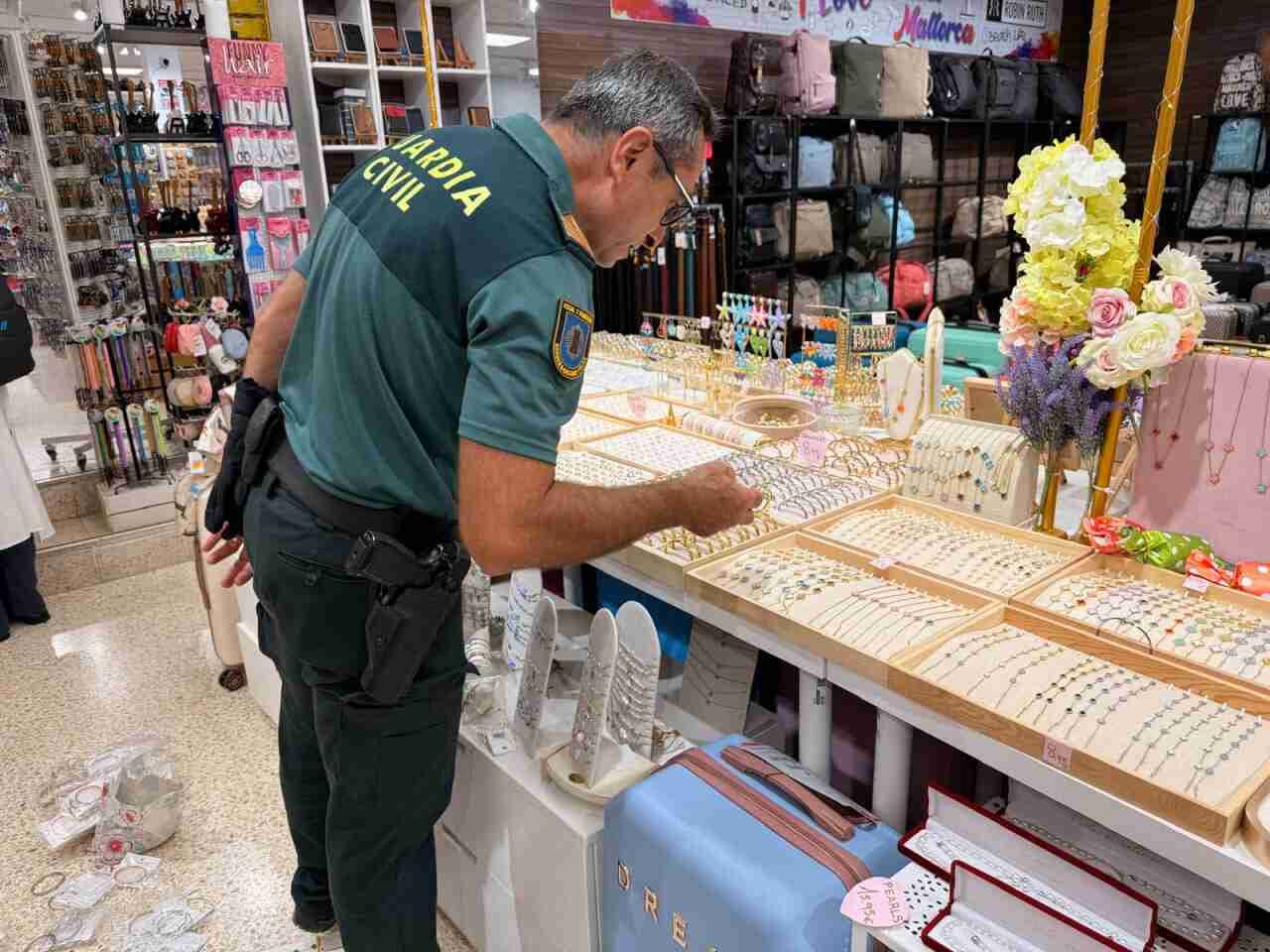 Un agente de la Guardia Civil de espaldas revisa muestras de bisutería dispuestas en los expositores de una tienda comercial de recuerdos