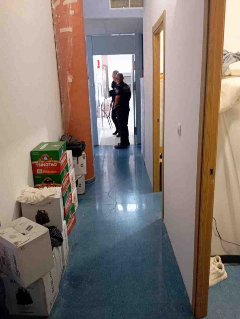 Agentes policiales recorriendo el pasillo interior de un restaurante con cajas apiladas de cerveza Tsingtao y materiales de almacén