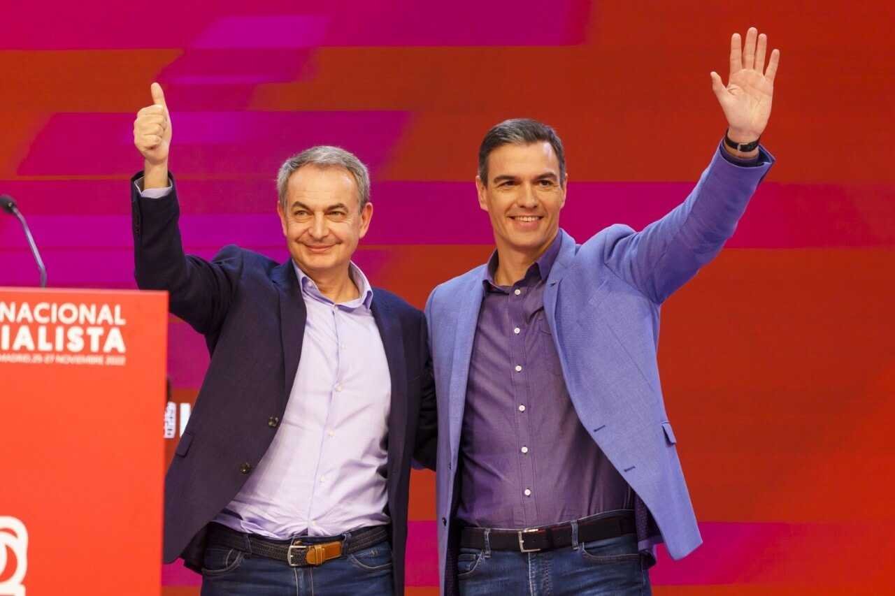 Fotografía de José Luis Rodríguez Zapatero y Pedro Sánchez saludando sonrientes desde un escenario