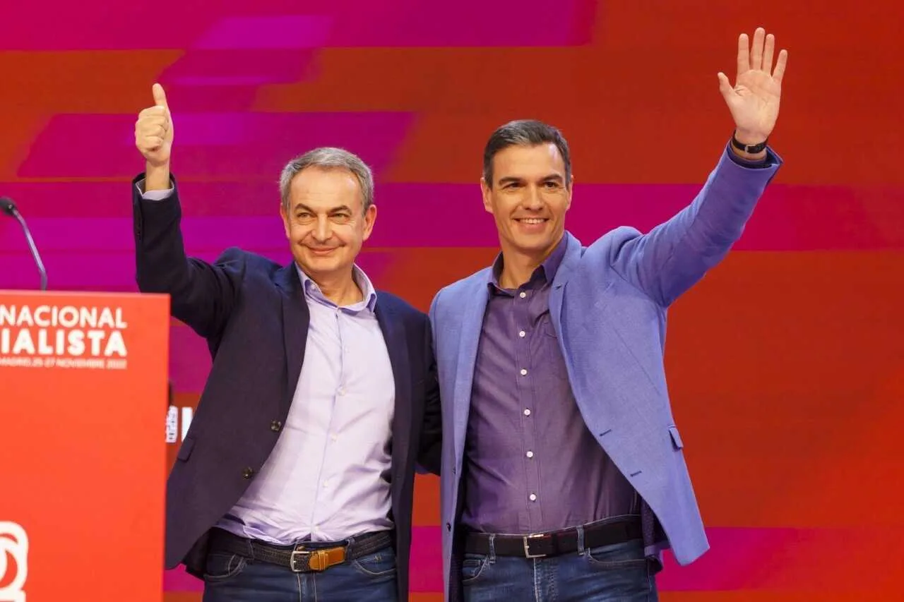 Fotografía de José Luis Rodríguez Zapatero y Pedro Sánchez saludando sonrientes desde un escenario