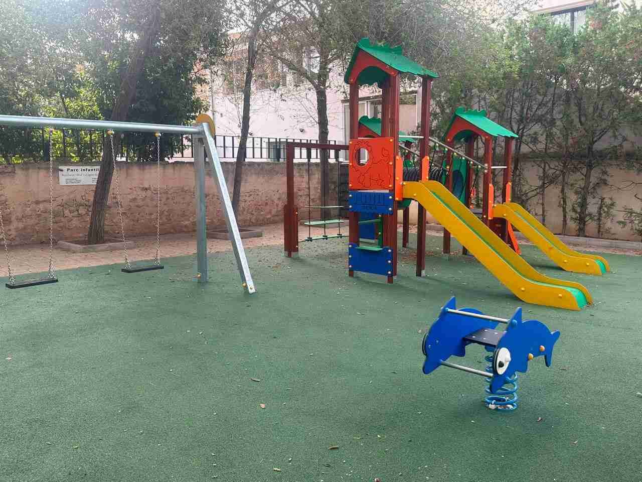 Parque infantil renovado con suelo verde amortiguador, toboganes de colores y columpios