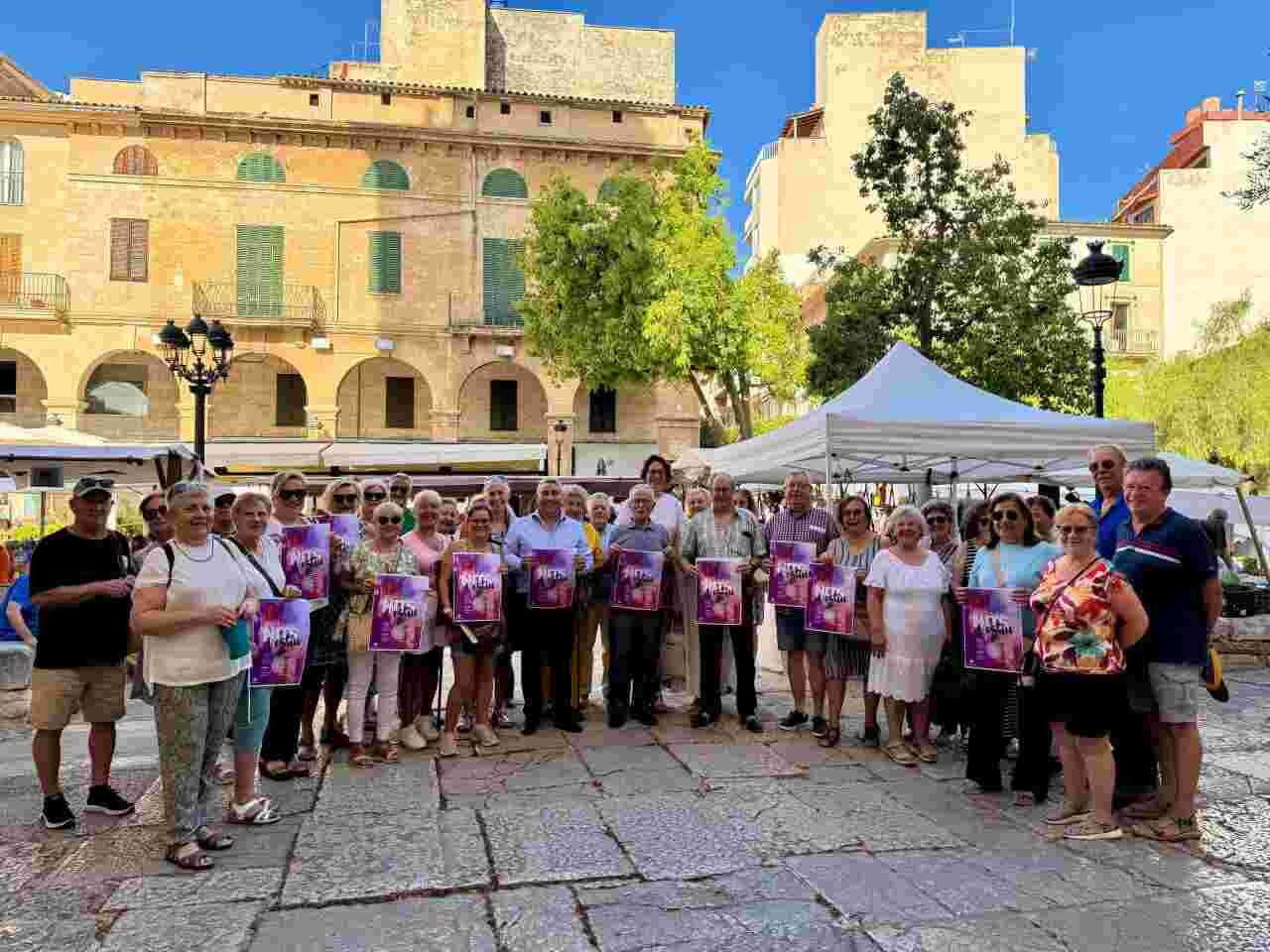 Grupo de personas mayores sosteniendo los carteles publicitarios del ciclo musical estival en una plaza pública de Inca