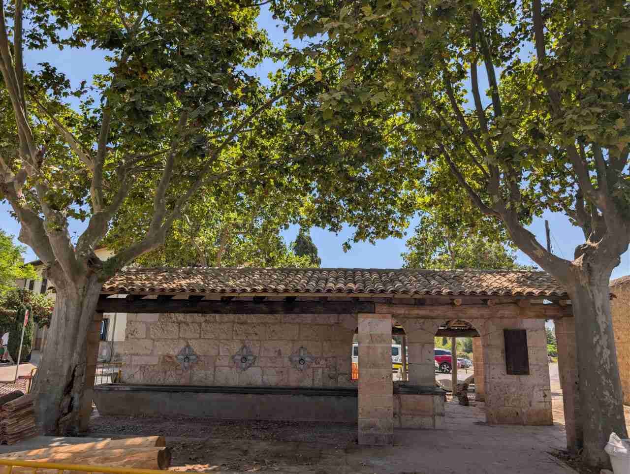 Estructura de piedra y tejado restaurado de la plaça des Pou Vell en Sant Llorenç des Cardassar entre árboles