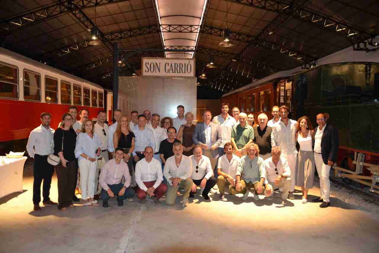 Foto de grupo de representantes políticos y hoteleros en el Museo del Ferrocarril de Son Carrió bajo un cartel de la estación