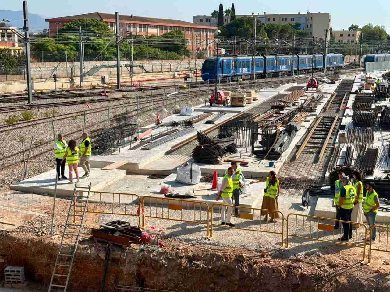 Vista panorámica de las obras de remodelación de los talleres de SFM en Son Rullan con un tren al fondo y autoridades inspeccionando los trabajos