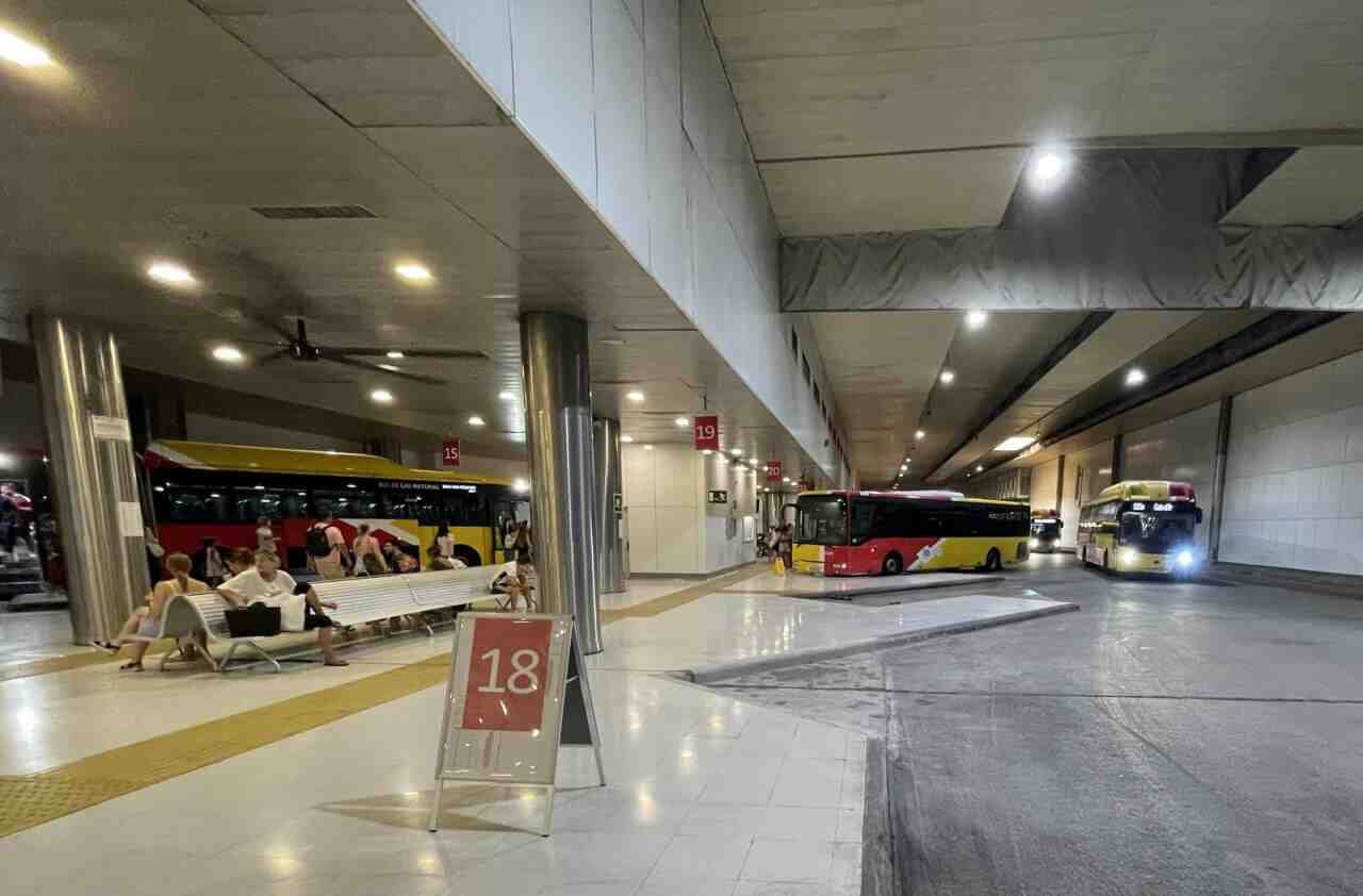Pasajeros esperando en los bancos junto a las dársenas numeradas de autobús de la Estación Intermodal de Palma