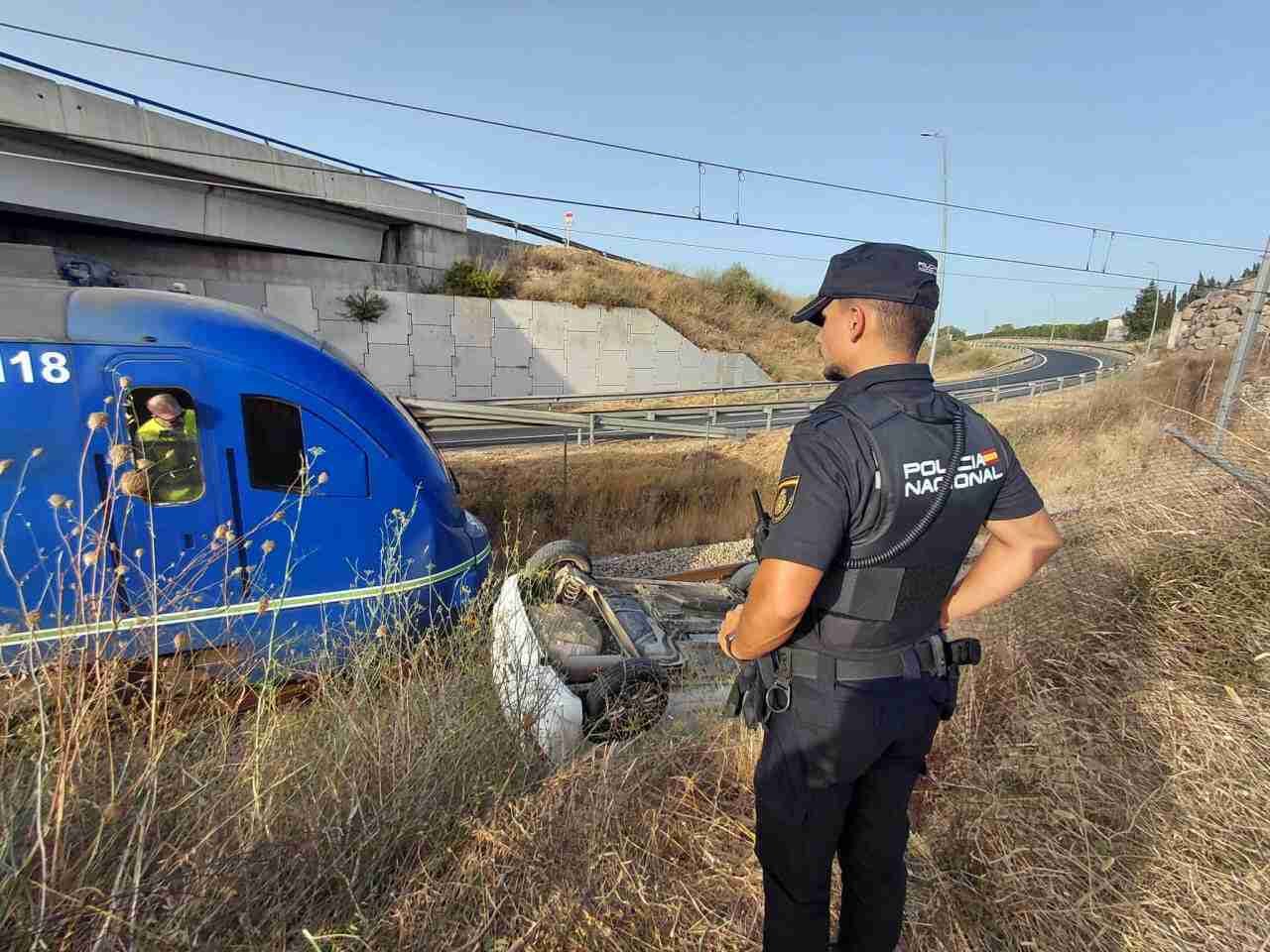 Un agente de la Policía Nacional observa el coche volcado sobre la vía junto al tren parado