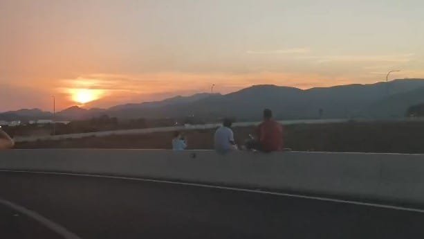 Espectadores contemplando el eclipse solar sentados en el murete de la carretera