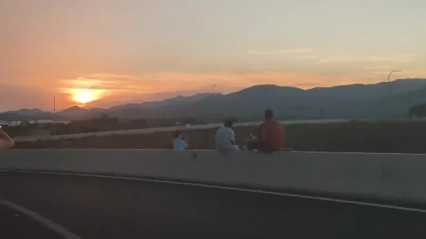 Espectadores contemplando el eclipse solar sentados en el murete de la carretera
