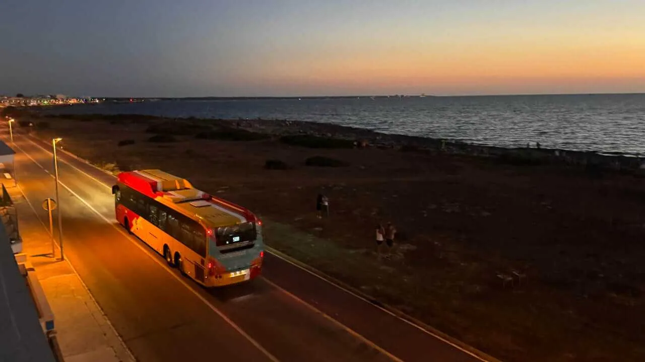 Un autobús interurbano de transporte público circulando por una carretera costera al atardecer durante el eclipse solar