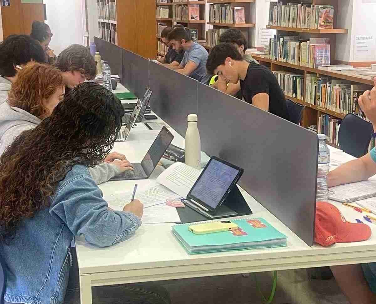 Jóvenes estudiando con portátiles y libros en la mesa central de la biblioteca de Manacor