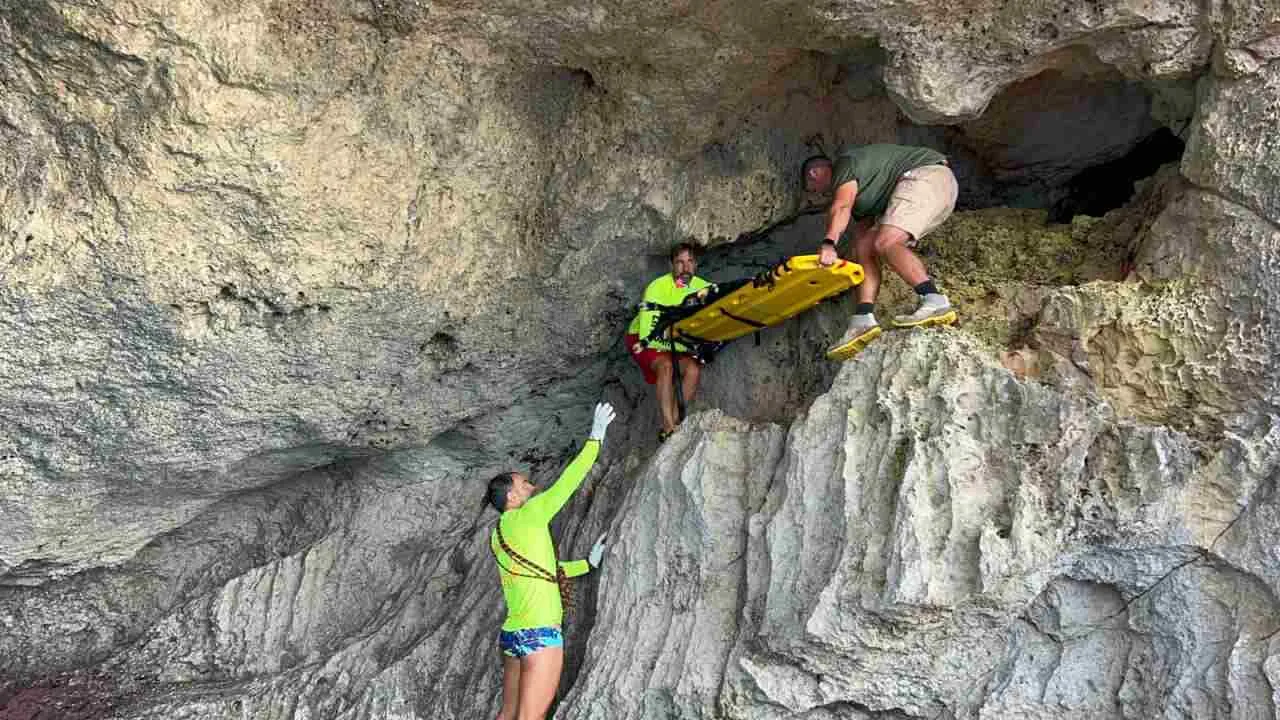 Socorristas y personal de rescate descendiendo con camilla por las rocas de una cueva en Cala Magraner