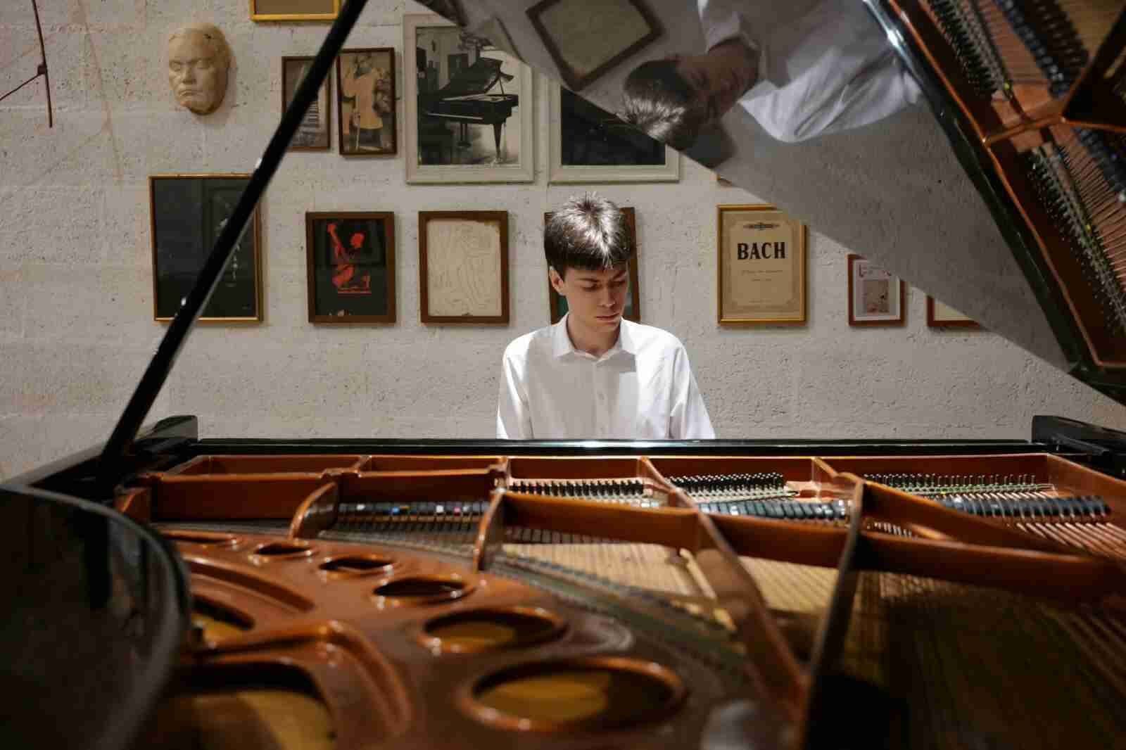 El joven pianista Agustí Aguiló Orfila al piano de cola con partituras y cuadros de fondo